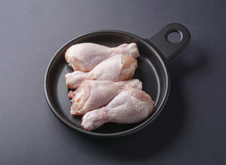 Poster - Close-up and top angle view of four pieces of raw chicken leg on a frying pan and black floor, South Korea
