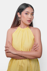 Wall Mural - Confident young Asian woman in a yellow dress standing and posing with arms folded.