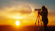© Anatthaphon - Silhouette of person using telescope during sunset, capturing the crescent moon and bright sun in breathtaking evening sky.