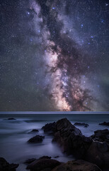 Constellation over ocean with rocks in foreground.