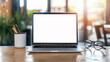 © Welle Photos - Close up of blank white screen laptop on table in modern office interior with creative station and cup, coffee mug, glasses and pencil pot at working desk with blurred background. Mockup for design.