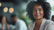 © Alina Tymofieieva - Portrait of a happy dark-skinned African American woman sitting at a desk in a work office. Young curly woman in business clothes indoors. Work concept. Lifestyle.