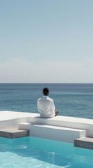 A man sits on the edge of an infinity pool overlooking the vast blue ocean