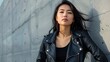 © Preecha - Detailed photograph of a fashionable Asian woman in a leather jacket, hands on hips, with a confident and stylish expression