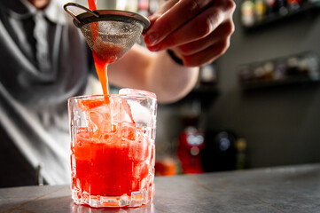 Wall Mural - A hand pours vibrant red liquid through a strainer into a glass, capturing the essence of mixology