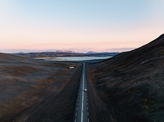 Wall Mural - View from above, stunning aerial view of a car on a beautiful road passing through a dramatic landscape with a lake and snowy mountains in the distance, Iceland