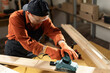 © Andrii Lysenko - professional female carpenter using wood polishing machine grinding sanding wooden board in her workshop