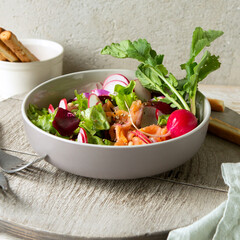 bowl of salad with baked beetroot, radish and salmon on light table