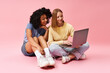 © LIGHTFIELD STUDIOS - Two diverse women in casual attire sitting on floor, engrossed in laptop.