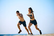 © master1305 - Dynamic and hard training outdoor session. Sportive young man and woman training on sandy beach, running under clear sky. Concept of sport, active and healthy lifestyle, body care, fitness