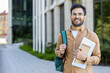 © Liubomir - Confident student standing outside modern university building. Young man wearing glasses, carrying backpack, holding books and laptop. Concept of education, college life, academic success, study