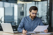 © Tetiana - Concentrated and serious young male accountant sitting in the office behind a desk and working with documents, checking and analyzing information and data