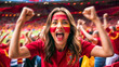 © rarrarorro - A young woman with Spanish face paint cheers enthusiastically at a soccer match in a stadium, wearing a red jersey. The background shows a blurred crowd of fans also celebrating.