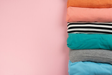 Wall Mural - close up of rolled colorful t shirt clothes on pink table background, travel and lifestyle concept