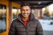© Markus Schröder - Portrait of a happy indian man in his 30s sporting a quilted insulated jacket while standing against stylized simple home office background