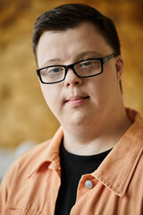 A young man with Down syndrome wears glasses and a peach-colored shirt as he looks into the camera.