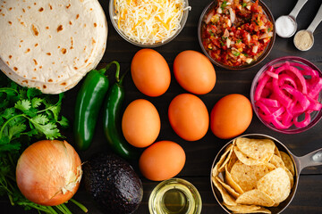 Wall Mural - Tex-Mex Migas Breakfast Tacos Ingredients: Eggs, tortilla chips, jalapeno peppers, flour tortillas, shredded cheese, and more on a wooden table