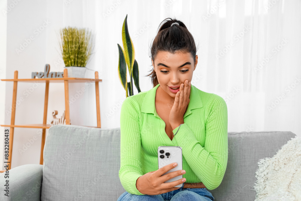 Surprised young woman using mobile phone at home