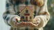 © bagoesanggito - Miniature house held in hands symbolizing home ownership real estate and property investment