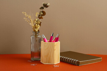 Wall Mural - Wooden holder with pens, notebook and vase of dried flowers on red table