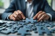 © Yuliia - closeup shot of a businessman meticulously fixing jigsaw pieces at his desk, symbolizing creativity, problem-solving, and implementation in the corporate world.