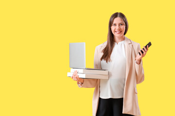 Wall Mural - Young pregnant businesswoman with laptop, folders and mobile phone on yellow background