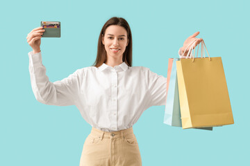 Poster - Beautiful young woman with shopping bags and credit card holder on blue background