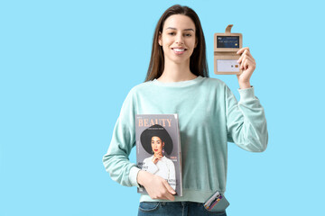 Sticker - Smiling young woman with magazine and credit card holders on blue background