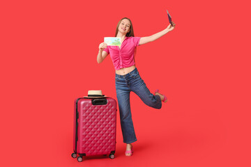 Sticker - Happy young woman near her suitcase with passport and gift voucher on red background. Travel concept