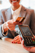 © Jose Calsina - Vertical. Unrecognizable woman paying the bill with a contactless credit card in a restaurant. Close up image of a female holding a creditcard and giving a payment transaction to the cashier dataphone