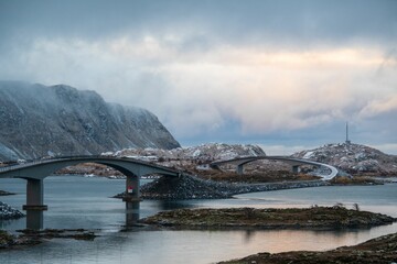 Poster - Scenic view of a bridge over a calm body of water with mountains in the background.