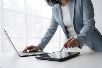 Focused businesswoman in a modern office, using laptop and tablet with stylus pen, showcasing professionalism and innovation