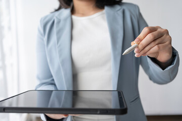 Confident businesswoman in blue blazer presents project with digital pen and tablet in modern office, showcasing expertise in technology and communication