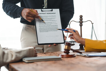 Wall Mural - Lawyers are reviewing and discussing a contract agreement at a wooden table with a gavel and scales of justice in the background