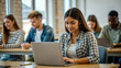 © NewFresh  - Young woman working on laptop in classroom. Group of people in the background.