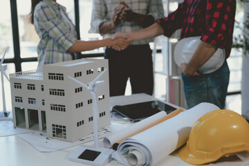 Wall Mural - team of architects is shaking hands in front of a model of a sustainable building with wind turbines