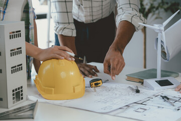 three architects are discussing a project with a model of a wind turbine and a model of a building, 
