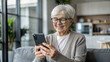 © NewFresh  - Smiling senior woman using mobile phone while sitting on sofa at home