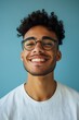 © Enigma - Cheerful young man with curly hair and glasses smiles against a blue backdrop, radiating happiness and positivity. Perfect for creative projects