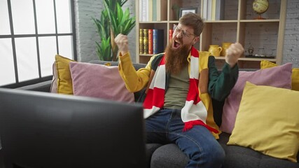 Wall Mural - Young bearded redhead man exulting while watching tv in a cozy living room setting