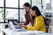 © David - Two cheerful asian office workers women cooperating on project, sitting at desk with laptop using calculator, finance accounting analytical concept.
