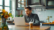 © chekart - A man is sitting at a table with a laptop and a cup of coffee. He is watching the morning news, smiling and enjoying the morning in the cozy kitchen