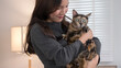 © snowing12 - A woman standing in a living room, holding her tortoiseshell cat close to her chest. The setting is calm and domestic