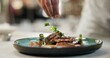 © CineLens2024/peopleimages.com - Hands, food or sprinkle on dish for fine dining, culinary school or luxury restaurant. Chef, healthy protein or spices on plate for seasoning, catering and hospitality for event in commercial kitchen