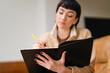 © Iryna - Woman Writing in Notebook With  Yellow Pen While Sitting on Couch