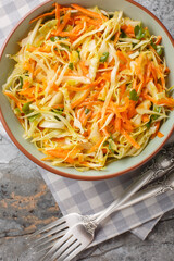 Wall Mural - White cabbage salad with fresh carrots and parsley dressed with vinegar and olive oil close-up in a bowl on the table. Vertical top view from above