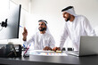© oneinchpunch - Arab men wearing traditional emirate clothing  working in the office - Middle eastern businessmen brainstorming at work