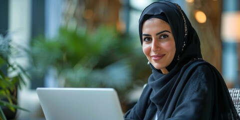 Wall Mural - Smiling Woman in a Black Hijab with a Laptop