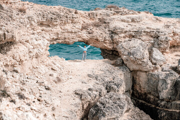 Wall Mural - A woman stands in front of a large rock formation with her arms outstretched. Concept of freedom and adventure, as the woman is embracing the natural beauty of the rocky landscape.