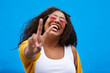 © Sanc/peopleimages.com - Happy, woman and portrait with peace sign in studio for gen z fashion, heart glasses and aesthetic style. Excited, girl and cool v icon with trendy eyewear, creative and opinion on blue background
